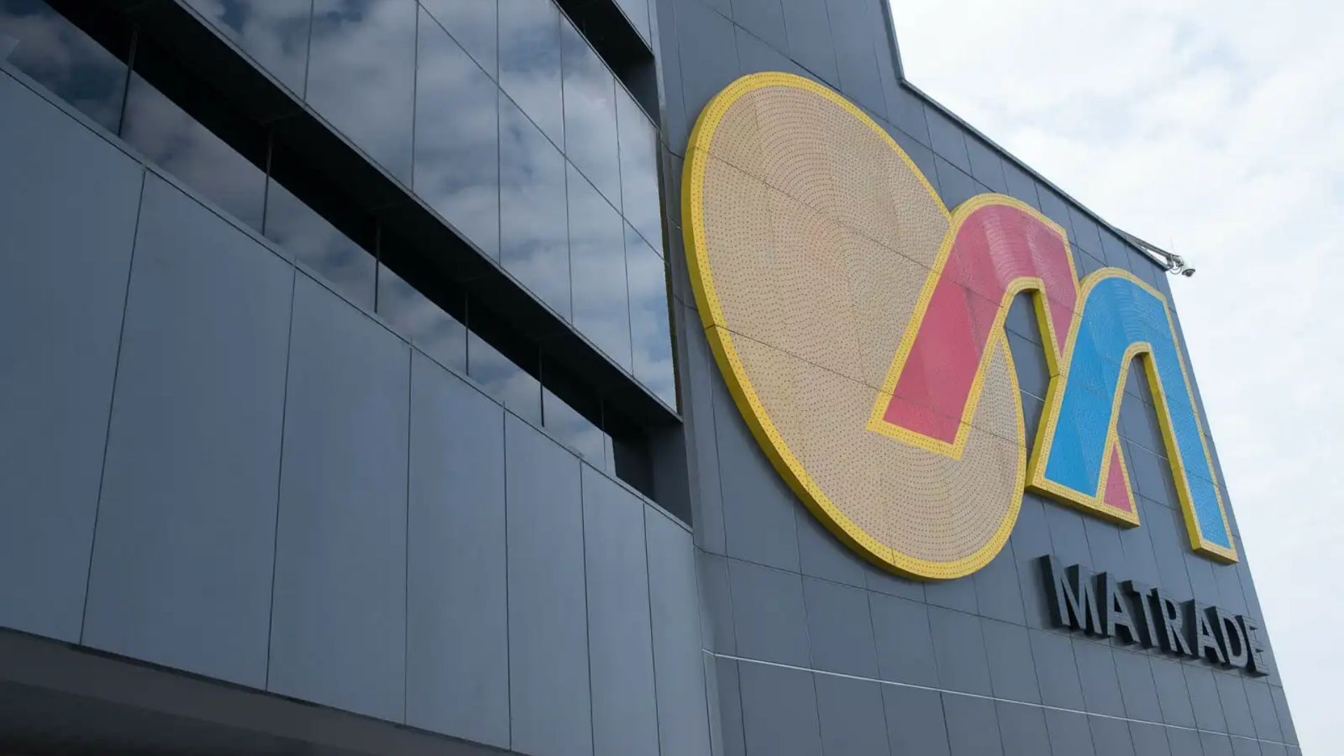 Fachada do edifício da Matrade na Malásia, com logotipo colorido refletindo o céu.